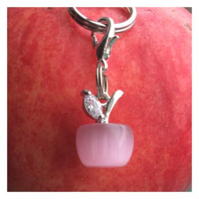 A charm that shows a pink apple with a silver stem and leaf on top of the apple. The background is red.