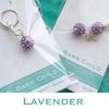 Two charms. One is a single purple and silver ball while the other is two purple and silver balls. They are both in their packaging that says Barn Child at the bottom. The word lavender, in teal, appears at the bottom of the image. The background is teal.