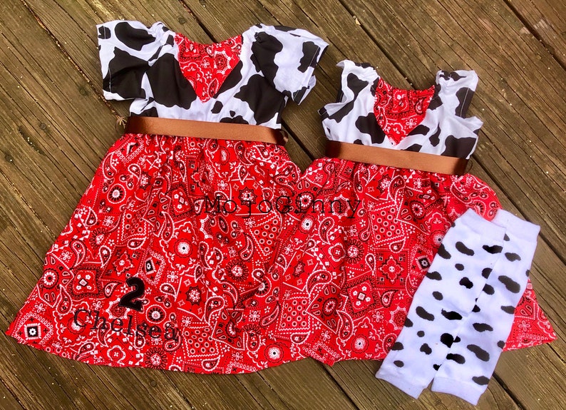 Two identical cowgirl costumes of different sizes beside one another. The top is a cow print and the bottom a paisley print.