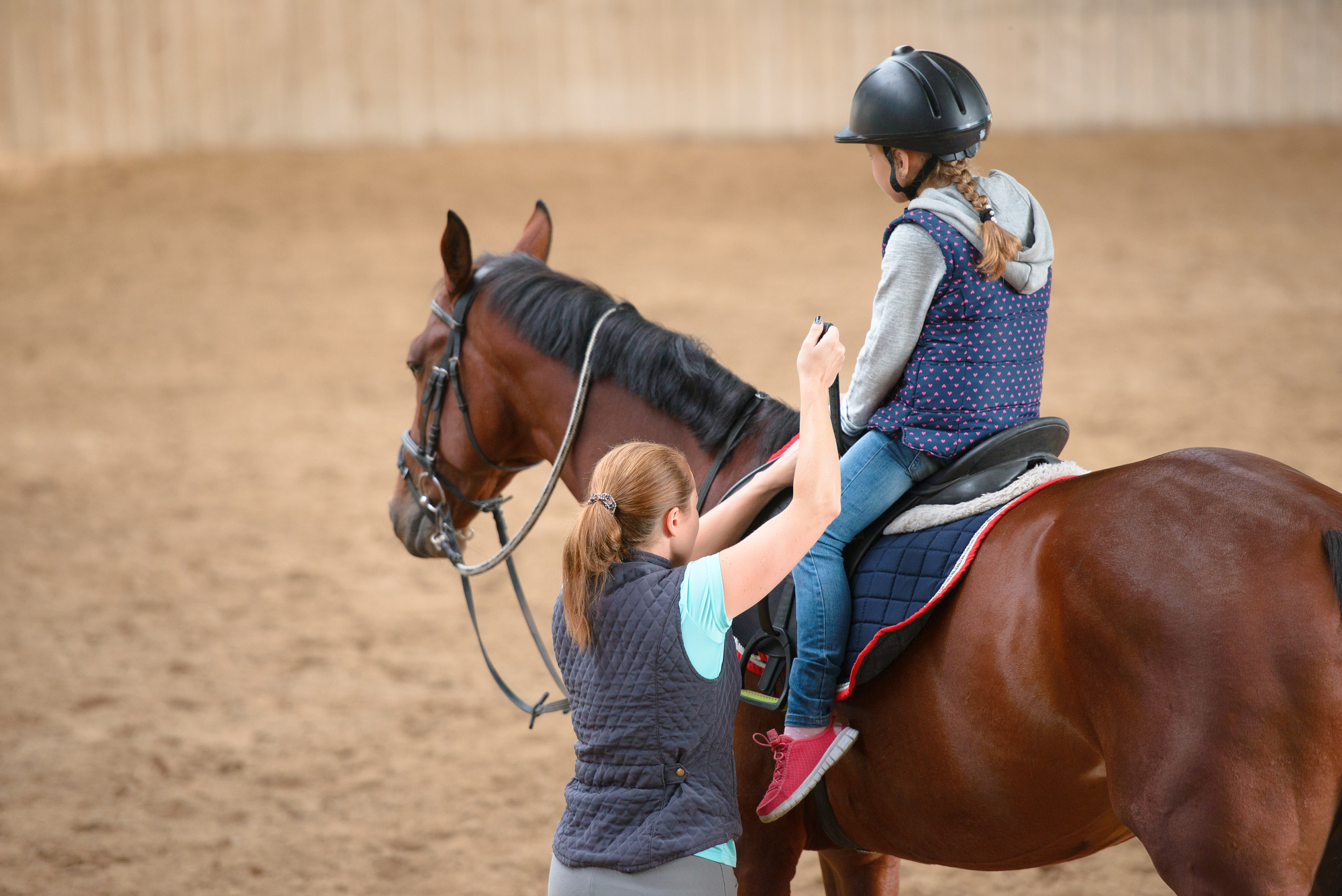 A girl on a horse having her stirrup adjusted by a woman standing on the ground.