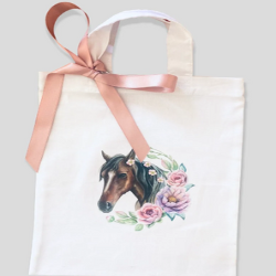 The horse themed party bags from NotJustPartyBags on Etsy. The creme cloth bags feature a bay horse head with a white stripe and flowers and greenery. There is a pink ribbon on the top.