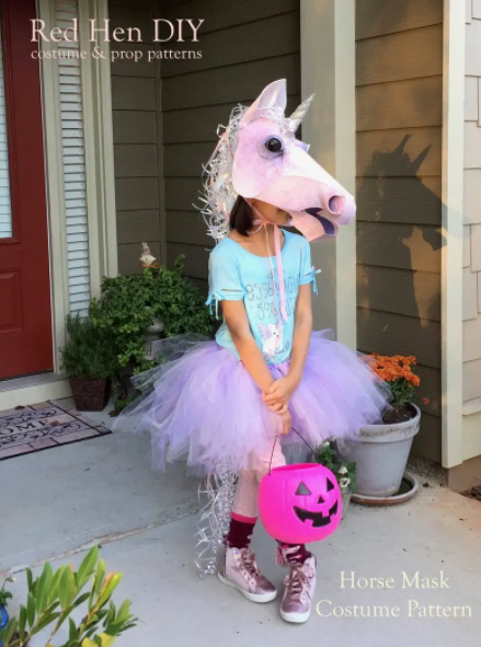 A young girl wearing a unicorn horse mask, a blue t-shirt, and a tutu.