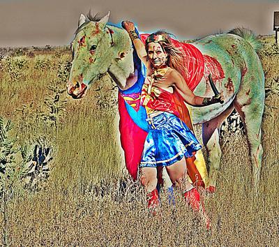 A girl dressed up as Wonder Woman standing next to a horse dressed up as Superman. Both have zombie makeup on them.