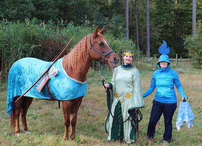 A horse dressed as Merida from the movie Brave standing next to two girls. One girl is dressed as queen Merida and another girl is dressed as the will o the wisp from the movie Brave.