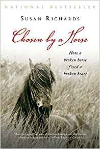 The cover of the book Chosen by a Horse. It has National Bestseller at the top in grey lettering then Susan Richards below that in black lettering and then Chosen by a Horse below that in red lettering. Below horse in black lettering are the words How a broken horse fixed a broken heart. The image on the cover shows a black and white image of a horse in a field with tall grass. At the bottom is something that can't be read in white lettering.