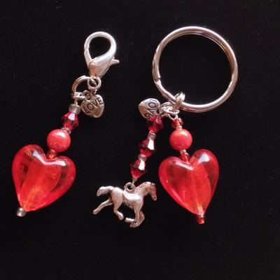 Two charms one that has a red heart and beads the other has a silver horse along with a red heart and beads.
