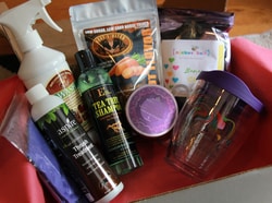 A box with red tissue paper that has items such as Aspire Thrush Treatment, Tea Tree Shampoo, and a Turvis Tumbler like cup with a purple lid and colorful horse on the cup. There are additional items that are hard to tell exactly what they are.