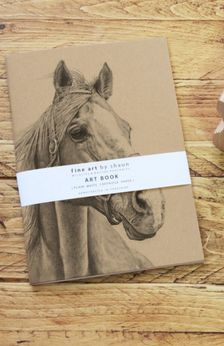 A sketch pad with a horse on the cover and pencils near the sketch pad and in a cup.