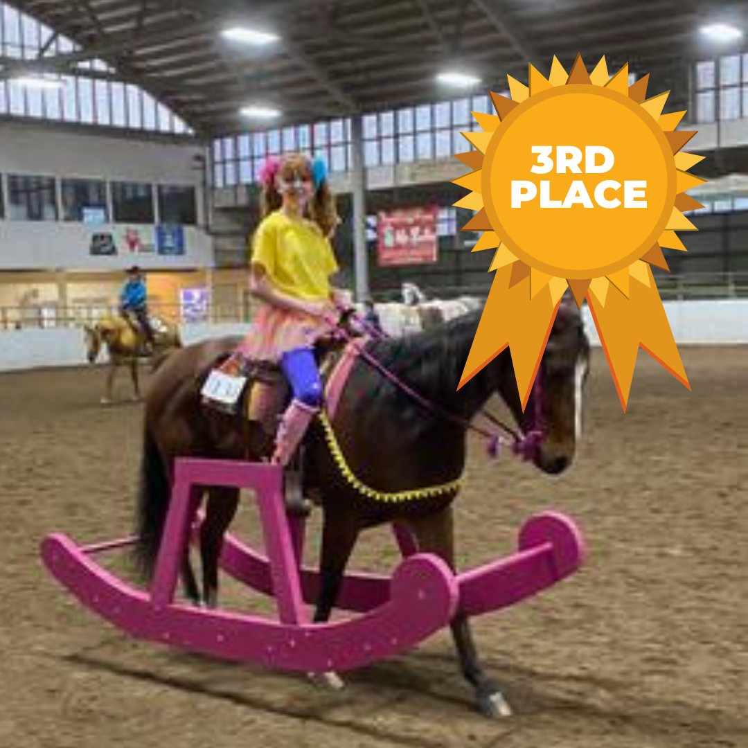 A horse dressed up to look like a rocking horse being ridden by a girl in a yellow shirt and a tutu to make her look like a little girl.