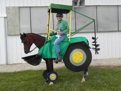 A girl dressed up as a farmer riding a horse in a tractor costume.