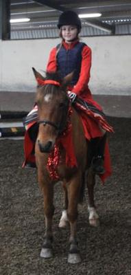 A girl wearing red riding a pony with devil horns on and red accessories.