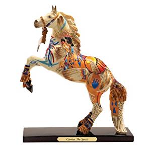 The Trail of Painted Pont collectable. It shows a cremello horse on a dark wood base that has a small plaque with the name of the horse. The horse is wearing a halter with tassels, dried grass attached to ornate clasps around the pasterns of all legs, and is decorated with images such as a Native American woman's face on the horse's neck, blue and red lines along its chest, an orange sunset like design on its hindquarters, and more.