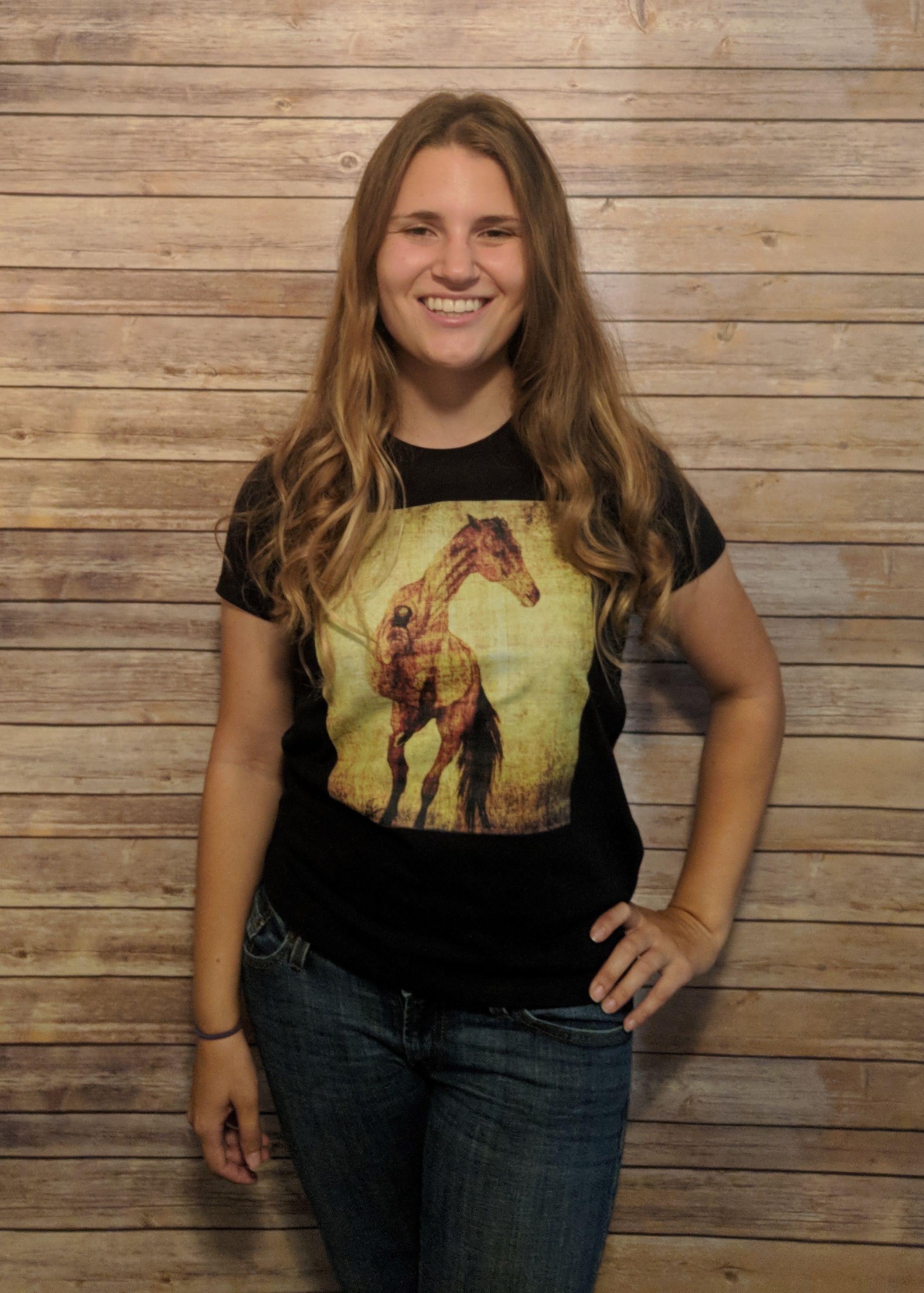 A girl wearing a t-shirt that shows a horse rearing and striking out.