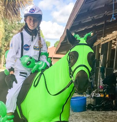 A girl in an astronaut costume on a horse in a alien costume.