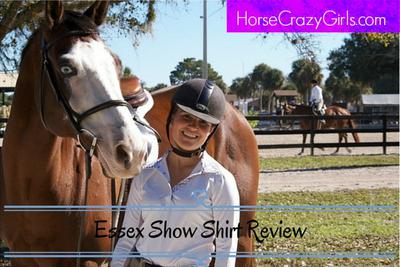 A girl in english show apparel including a white Essex horse show shirt standing next to a horse in english tack. In the background is a horse and rider along with an arena with a fence.The words Essex Show Shirt Review is in black lettering at the bottom of the photo with blue lines above and below it. At the top in a purple box in white lettering is HorseCrazyGirls.com