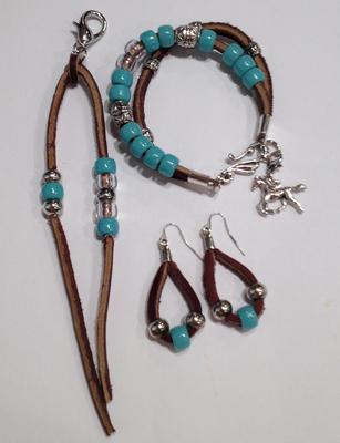 Three pieces of jewelry. One is a bracelet that is made of two pieces of brown felt and has blue, clear, and silver beads along with a silver horse charm. Another is a set of earrings made of brown felt with a blue bead in the middle and two silver beads on either side of the blue bead. The third piece is a piece of brown felt with blue, silver, and clear beads.