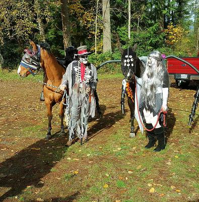 Two people dressed up as zombies with two horses one of which is dressed up as a spider and another is in a costume that is not clear what it is.
