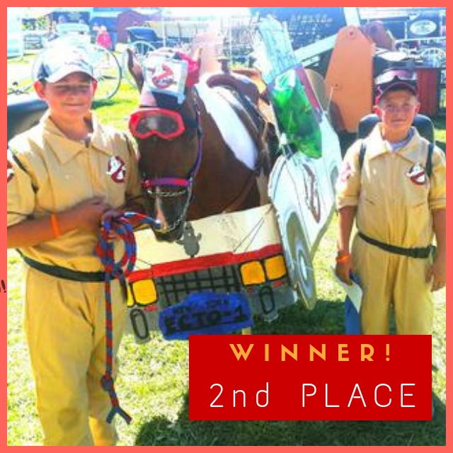 A horse dressed up as the van from the movie Ghostbusters standing between two boys with Ghostbuster costumes on.