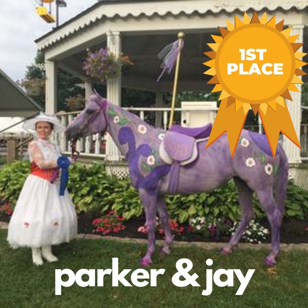 A horse painted purple with painted flowers on it as well being held by a woman dressed up as Mary Poppins. The horse has a pole attached to its saddle to make it look like a carousel horse.