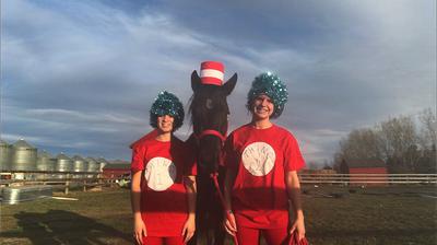 A horse wearing a red and white striped hat alongside two kids dressed in thing one and thing 2 shirts with blue wigs on.