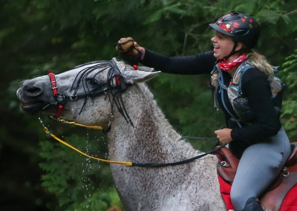 Image from ride like an athlete of a woman putting water on a grey horse with a sponge