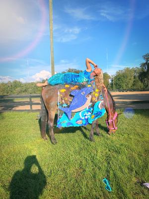 A woman dressed like a mermaid laying on her horse who is dressed up to look like the ocean.