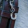 A silver horseshoe charm with sparkles on a brown bridle. The bridle is on a grey horse.